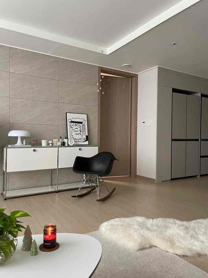 White and natural toned living room featuring white sideboard, black armchair, and lit candle on a simple, cozy setting