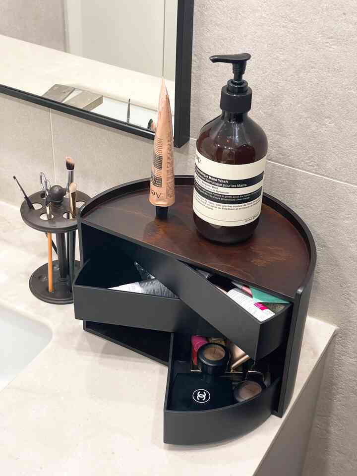 Wood tone and black rotating drawer vanity in a powder room, combining practicality with a French country style organizer