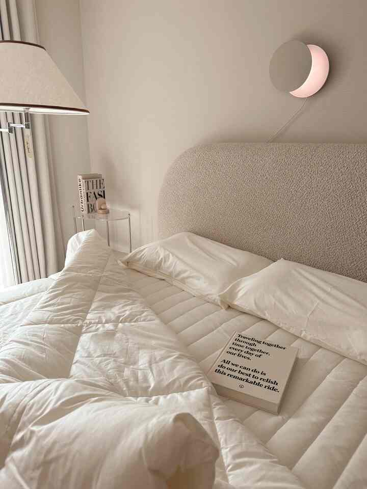 ベージュと白の色調の寝室、丸みを帯びたヘッドボードと柔らかな寝具が印象的な雰囲気のインテリア