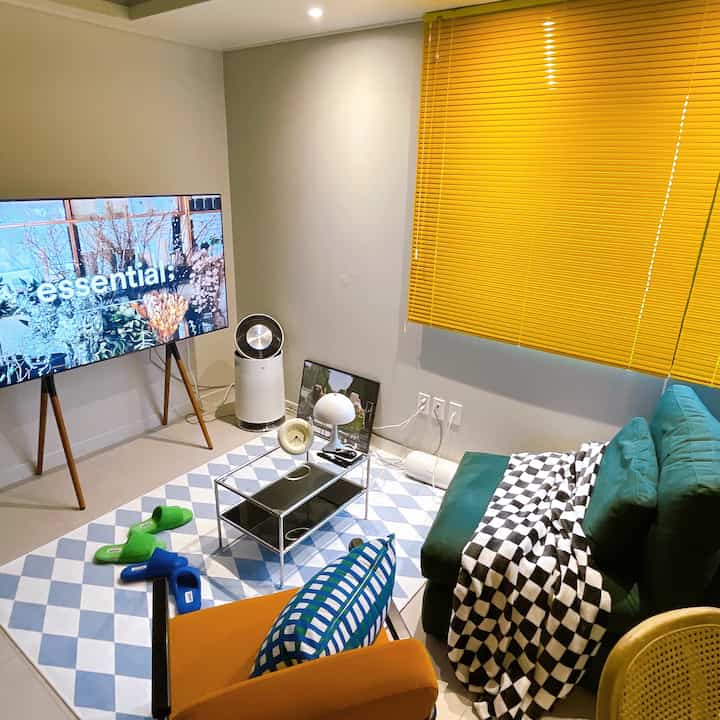 Mid-century modern living room with yellow blinds, green sofa, orange chair, and minimalist coffee table