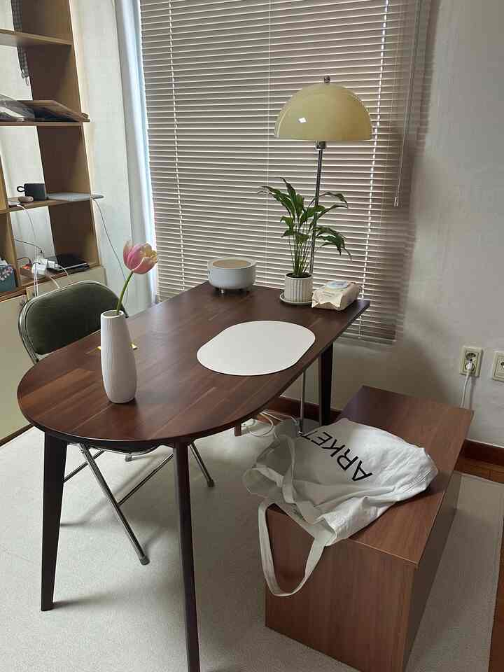 ベージュと木目調が調和したダイニング、ダークウッドのテーブルとベンチ、照明、植物が配置された雰囲気のある空間