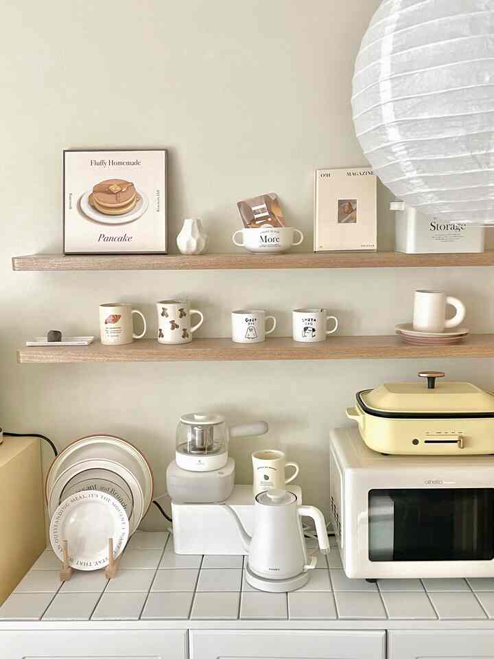 White and wood tone kitchen featuring wall shelves with neatly displayed mugs and plates, creating a cozy interior