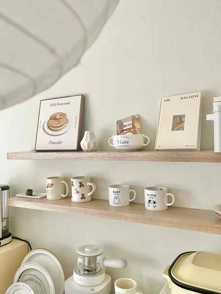 White and beige toned kitchen featuring shelves with various mugs and plates arranged in a cozy home cafe style