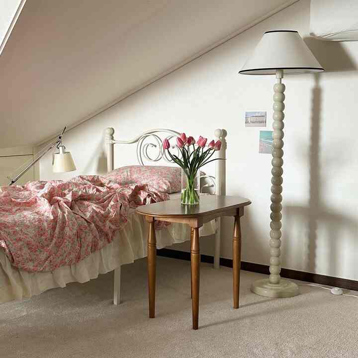 白とナチュラルカラーの寝室、花瓶のある木製テーブルと特徴的な勾配天井が印象的な落ち着いた空間