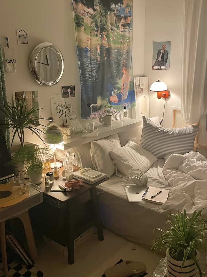 ナチュラルな色調の寝室、ソファベッドとナイトテーブル、多数の植物と暖かい照明が配置された雰囲気のあるインテリア