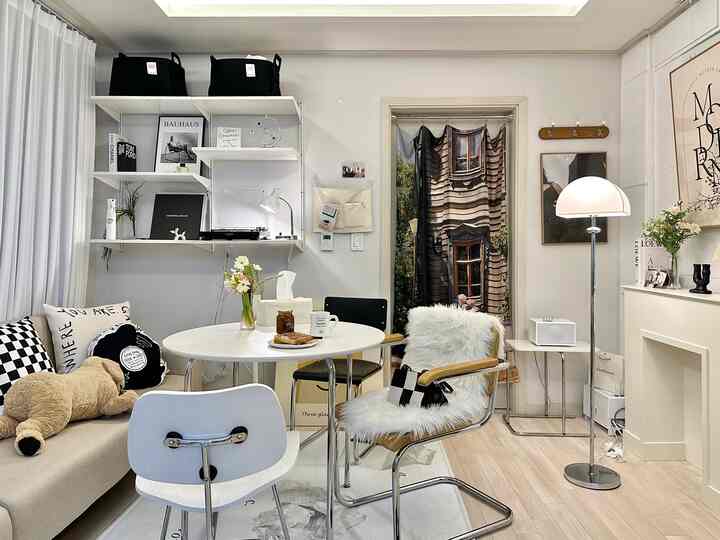 Natural modern toned living room featuring a round dining table with mixed chairs, floor lamp, posters, and decorative curtains creating a cozy ambiance