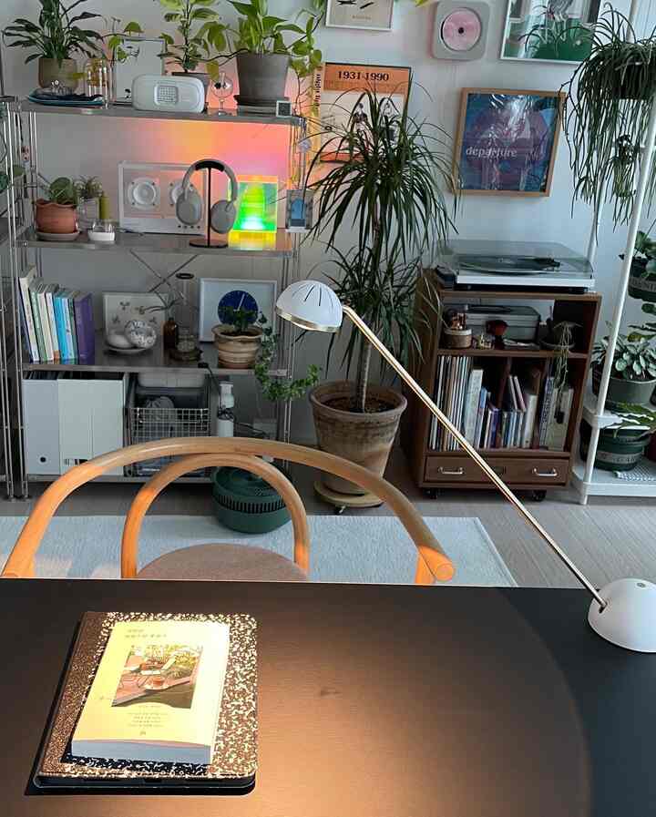 White-toned home office with wood-tone furniture, featuring plants and retro music equipment creating a cozy atmosphere