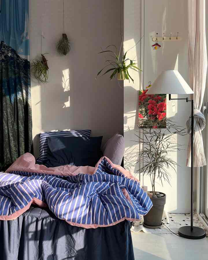 A blue and natural tone studio apartment bedroom featuring striped bedding and various pillows, creating a cozy atmosphere
