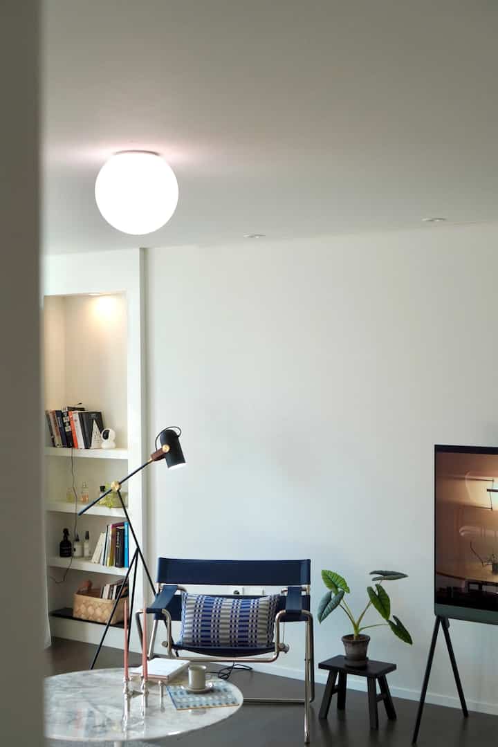 Modern living room with white walls and ceiling, featuring a blue armchair, marble coffee table, and a plant accent