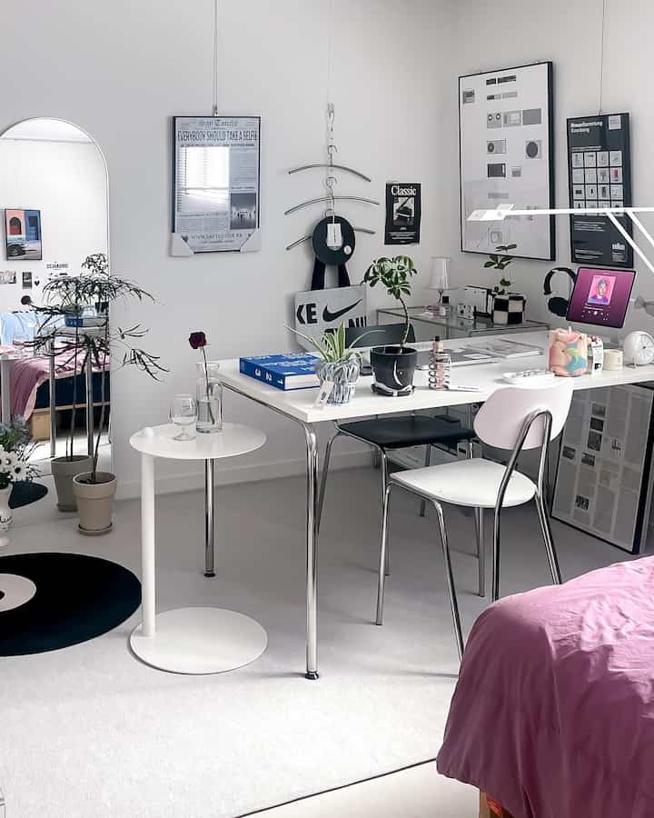 White and black toned studio bedroom with home office, featuring a modern desk and plants in a clean workspace