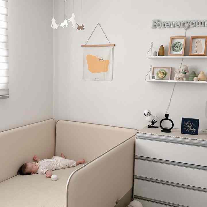 Beige and white toned kids' room featuring a bed, mobile, and cozy baby accessories