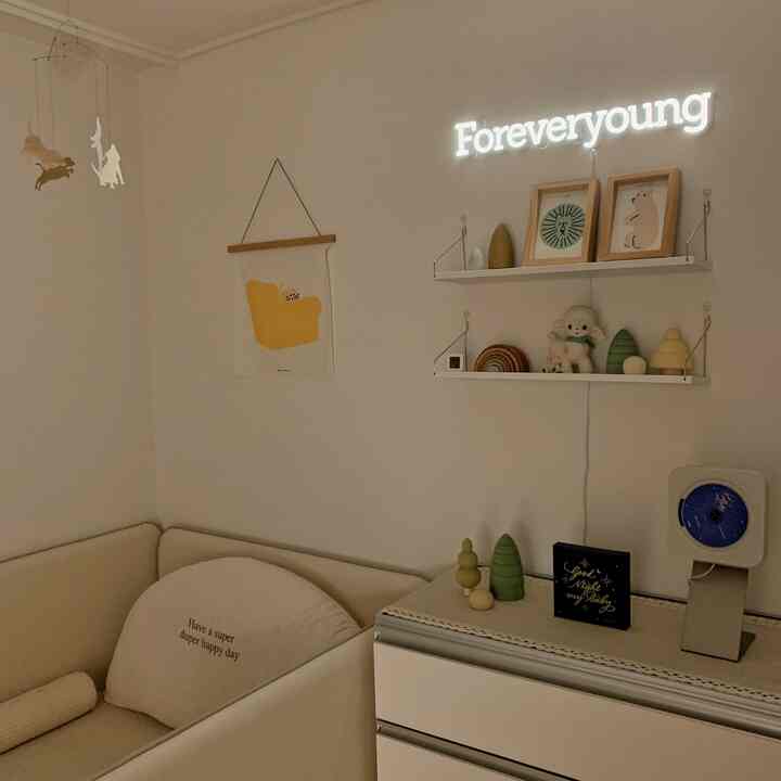 Beige and white toned kids' room corner featuring baby mobile, toys, posters, and warm lighting creating cozy atmosphere