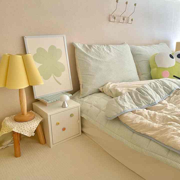 Beige and soft green toned bedroom featuring bed, yellow table lamp on wooden stool, creating cozy ambiance