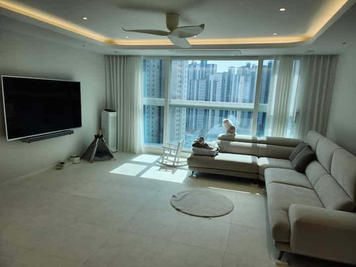 Bright white and beige-toned living room featuring a large sectional sofa and a cat, with a bright and simple atmosphere