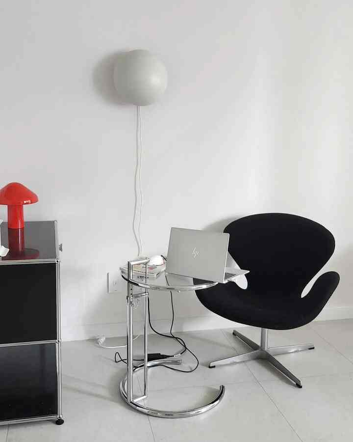 White and black toned living room featuring a minimal black lounge chair and glass side table with laptop, creating a clean remote work setup