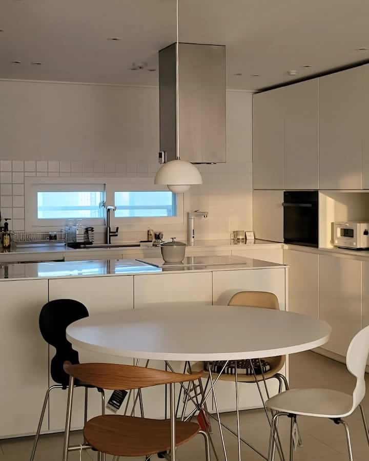 Modern kitchen with dominant white and wood tones, featuring a round dining table and mixed-color chairs creating a warm atmosphere