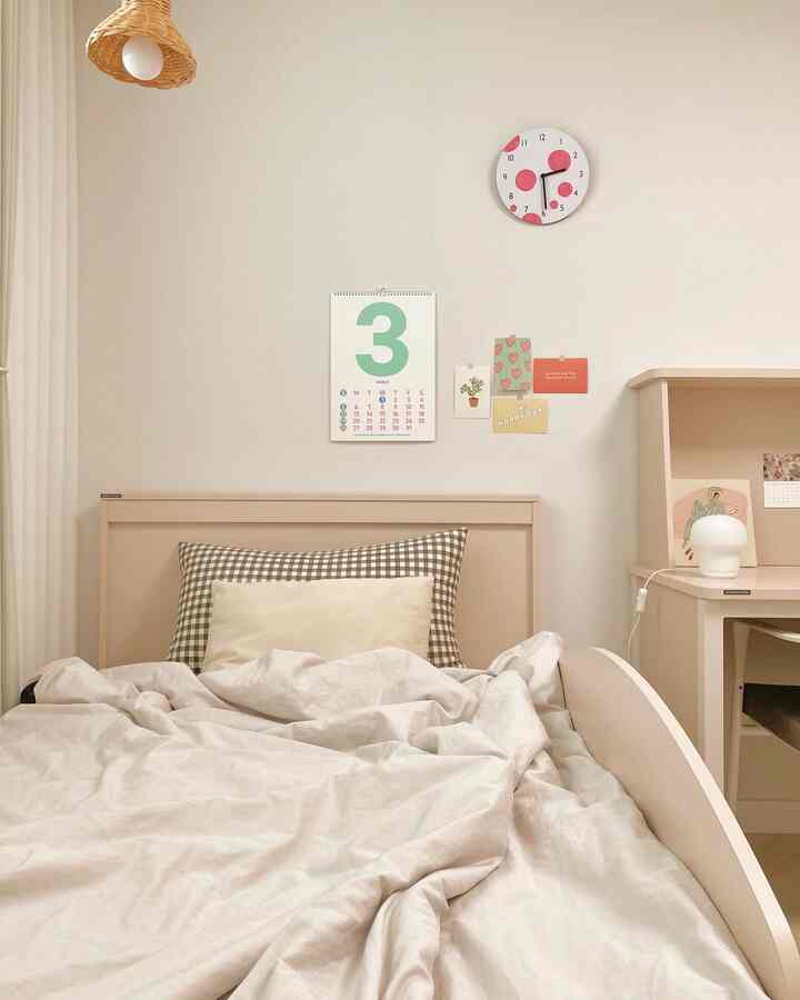 ホワイトとベージュのトーンの子供部屋、ベッドとデスク、壁に時計とカレンダーが配置された雰囲気のある空間