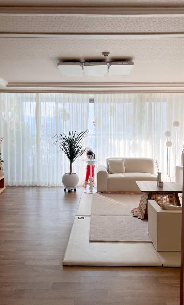 White and beige toned living room featuring white sofa, beige rug, and plant with cozy atmosphere