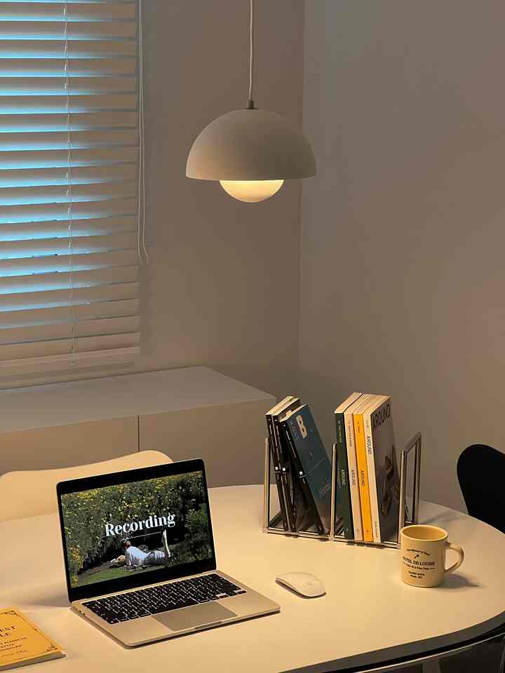 White-toned home office space featuring a dining table with laptop, magazine rack, and pendant light in a neat interior