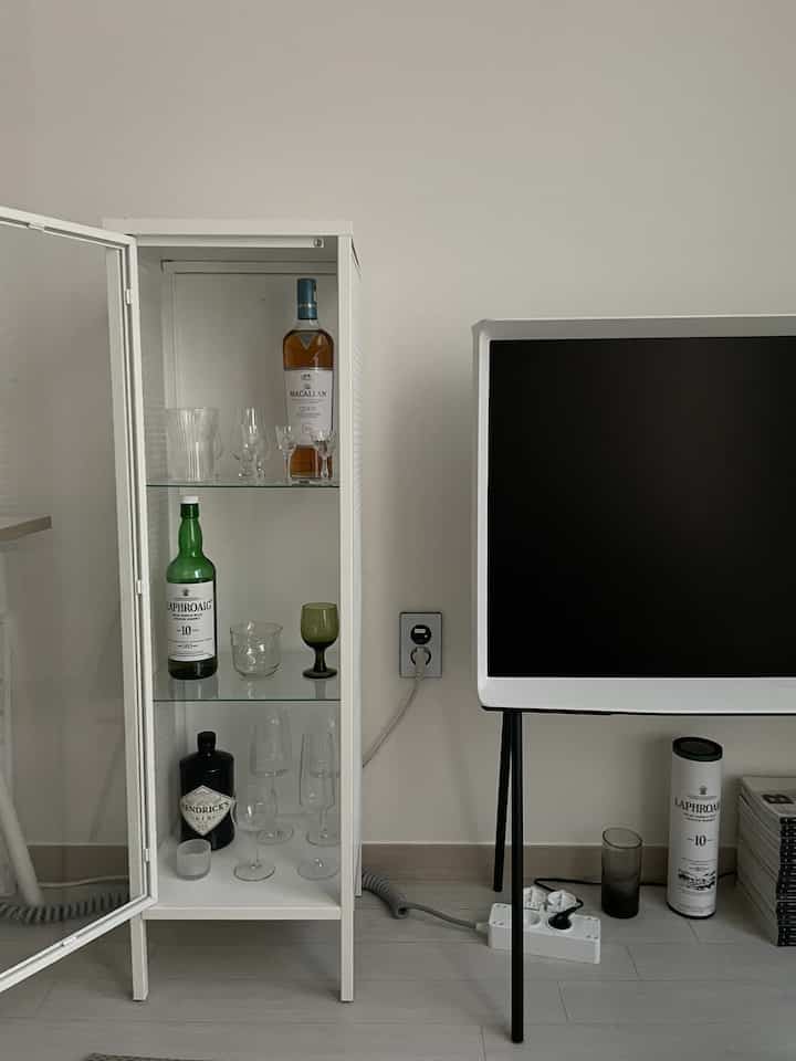 White-tone living room featuring a glass display cabinet and TV stand, creating a modern and clean home bar setup