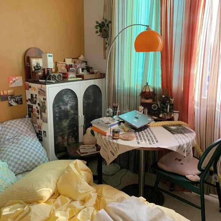 Small bedroom with warm yellow and orange tones, featuring a round dining table and cozy lighting