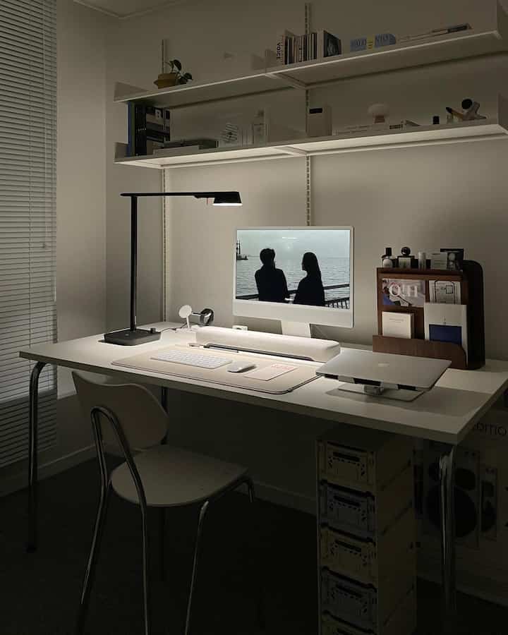 White-toned home office space featuring a desk with a computer monitor and desk lamp, creating a clean workspace
