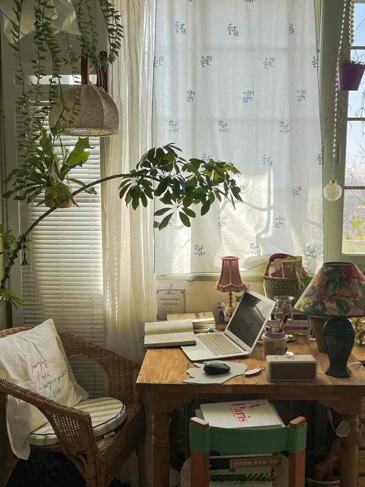 Natural wood tone home office with plants, cozy remote work setup by window with blinds and soft curtains