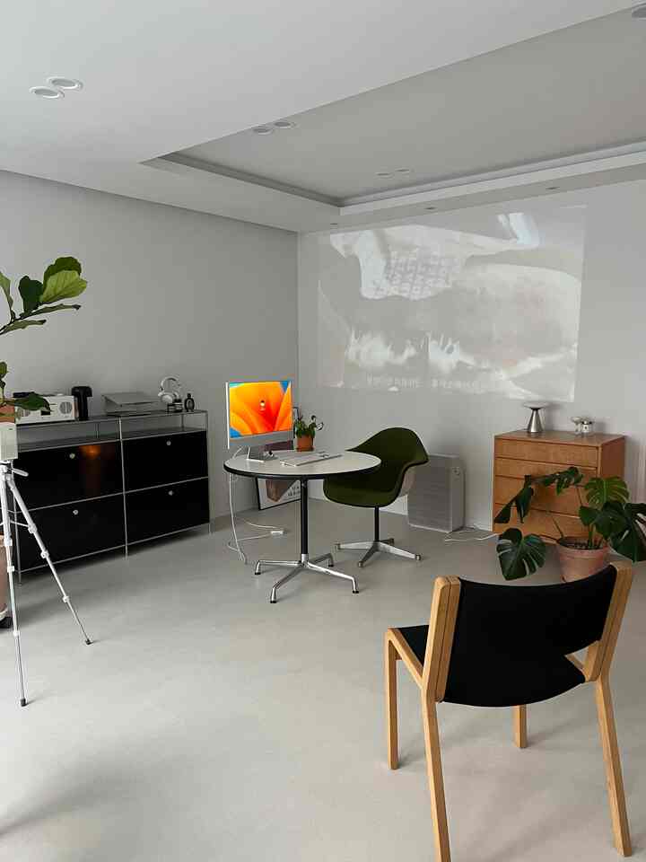 White-toned studio apartment home office featuring a round table, modern furniture, and plants with a clean, minimalist atmosphere