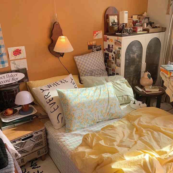 Yellow and brown toned bedroom featuring vintage wall sconce, multiple pillows, and various objets creating a cozy atmosphere