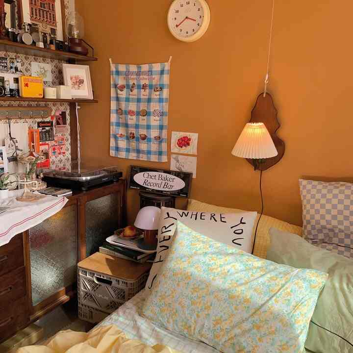 Warm orange-walled living room featuring vintage furniture, cozy floral pillows, and artistic decor creating a comfortable retro atmosphere