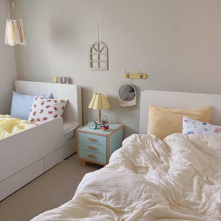 黄色がアクセントの子供部屋、二つの子供用ベッドと木製家具が配置された温かく居心地の良いインテリア