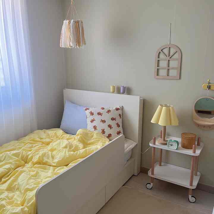 クリーム色の壁と白いベッドが配置された子供部屋で、黄色い寝具とウッドトーンの家具が温かみのある雰囲気を演出するインテリア