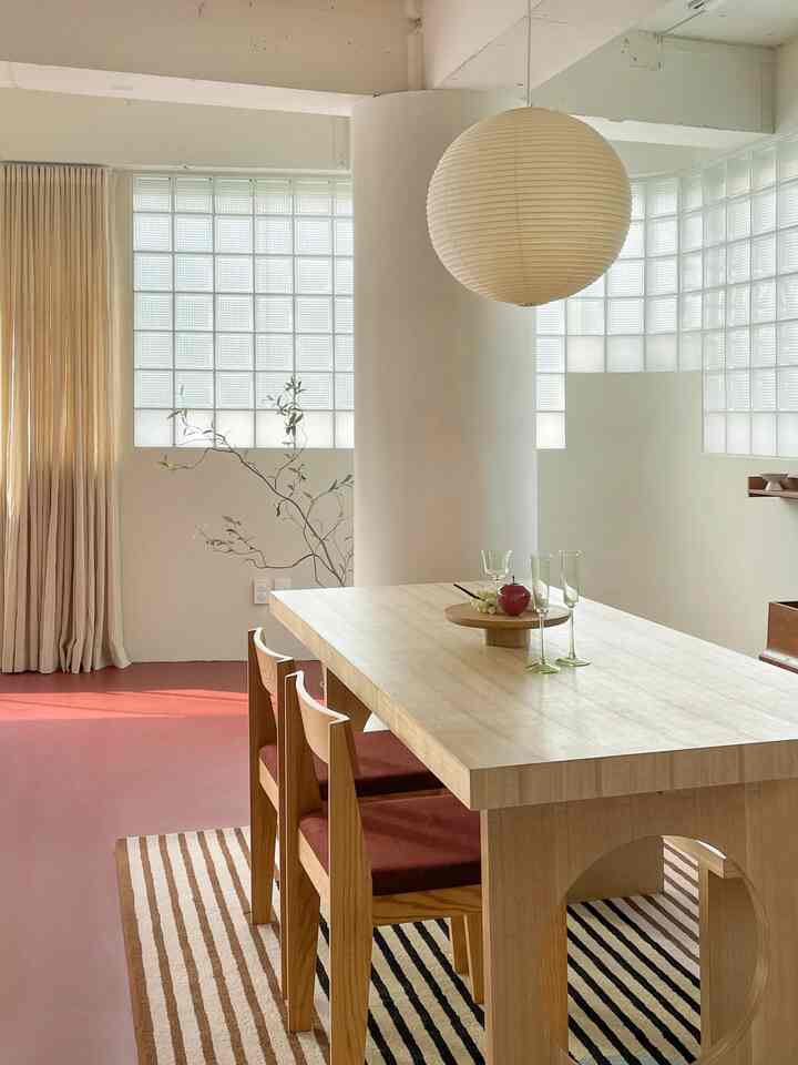 ナチュラルな色調のダイニング、木製のダイニングテーブルと赤いクッションチェア、クリーム色のカーテン、丸いペンダントライトが配置された雰囲気のある空間