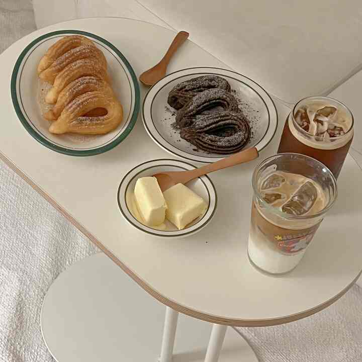 Soft beige-toned home cafe table featuring croissants, chocolate pastries, and two glasses of iced coffee, creating a cozy atmosphere