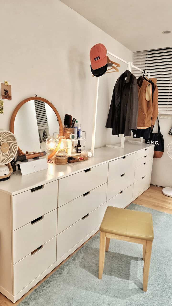 ホワイトとウッドトーンが調和した広いウォークインクローゼット、ドレッサーと丸い鏡が配置され、清潔で居心地の良い衣装部屋のインテリア