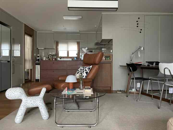 Modern living room and kitchen space in brown and gray tones, featuring a recliner and glass coffee table centrally placed