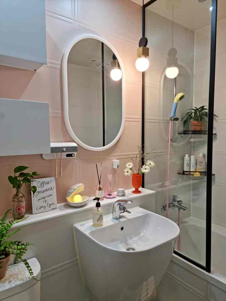 Bathroom with pink-toned walls, white basin sink, oval mirror, ambient lighting, and assorted bathroom accessories creating a cozy atmosphere