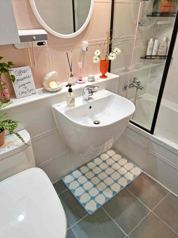 白とグレーの色調のバスルーム、洗面台とトイレ、バスマットと花瓶が配置された清潔で温かみのあるインテリア