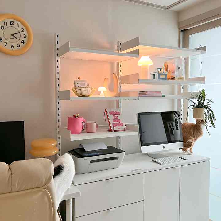 Modern white-toned home office space with two cats, featuring clean shelves, desk, and soft lighting creating a cozy atmosphere