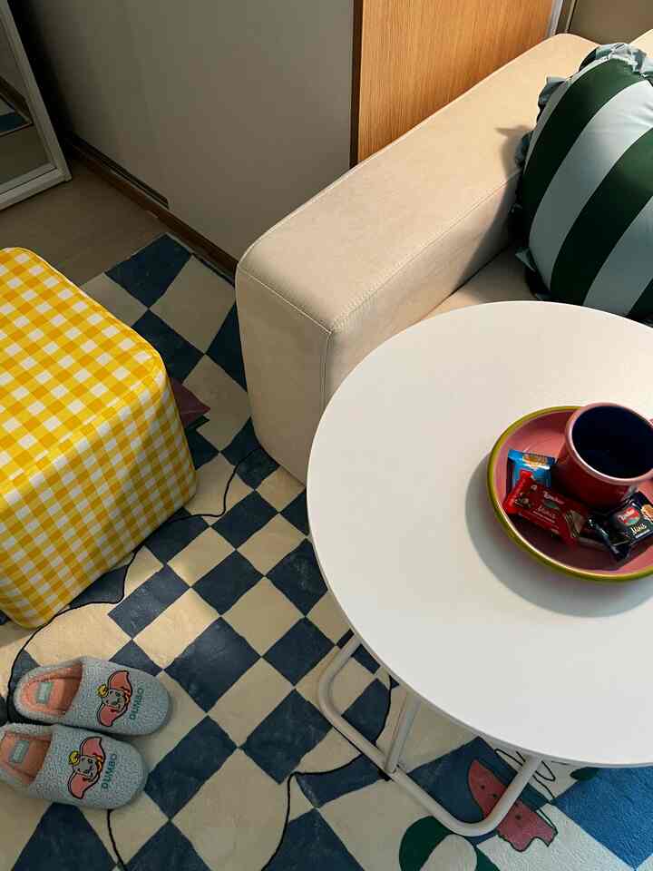 Blue checkered patterned rug with white round side table and yellow check stool, creating a cute and cozy compact interior space