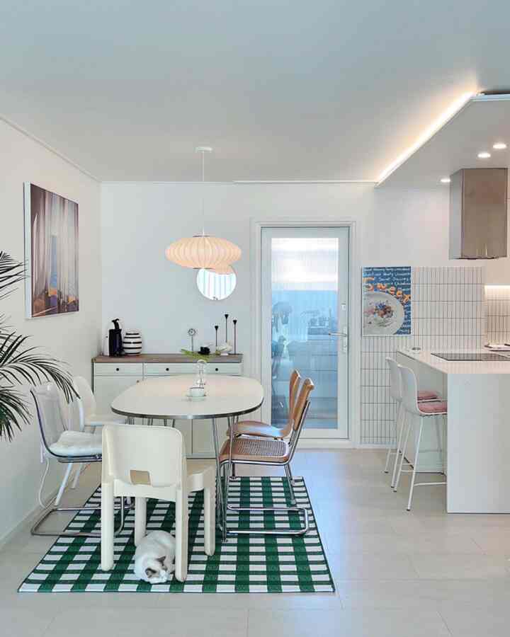 白と緑のトーンのバルコニーに面したキッチンダイニング空間、多様なダイニングチェアとペンダント照明が配置されたモダンなインテリア