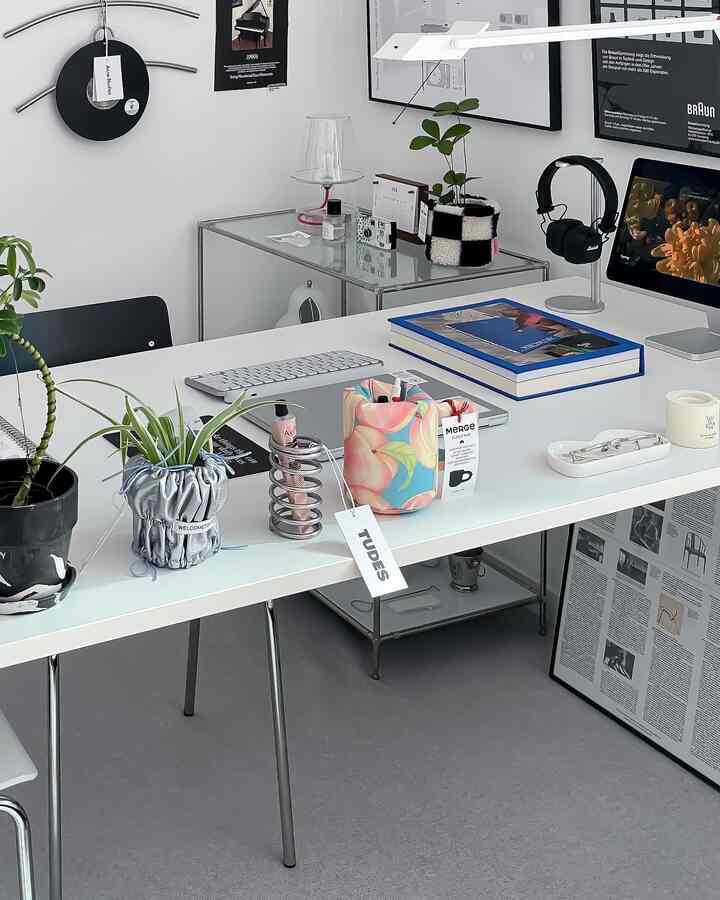 White and gray toned home office space featuring a neat desk, monitor stand, headphones, and plants creating a modern work environment