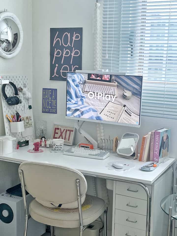 White-toned compact home office featuring a white desk, office chair, monitor arm, and posters in a tidy workspace