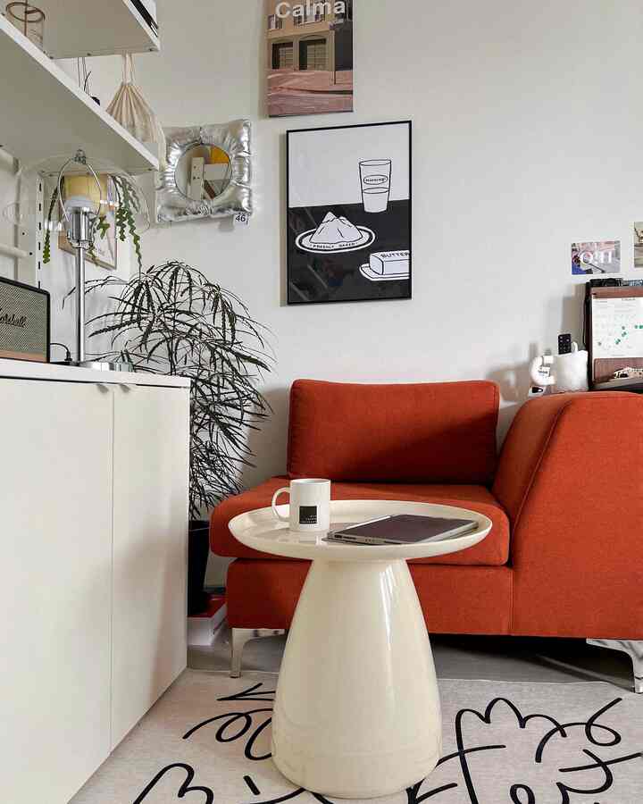 Living room with white walls, an orange single sofa, and a white round side table creating a cozy atmosphere