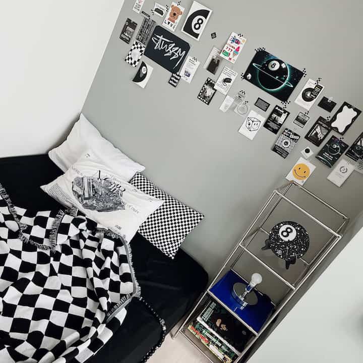 A modern small bedroom in white and gray tones featuring a black sofa bed with checkerboard patterned blanket and pillows