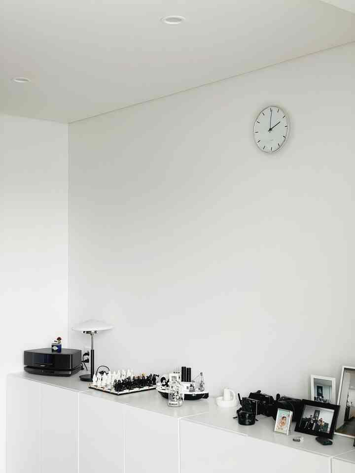 White-toned interior with wall clock and minimalist home office setup featuring lighting on cabinets