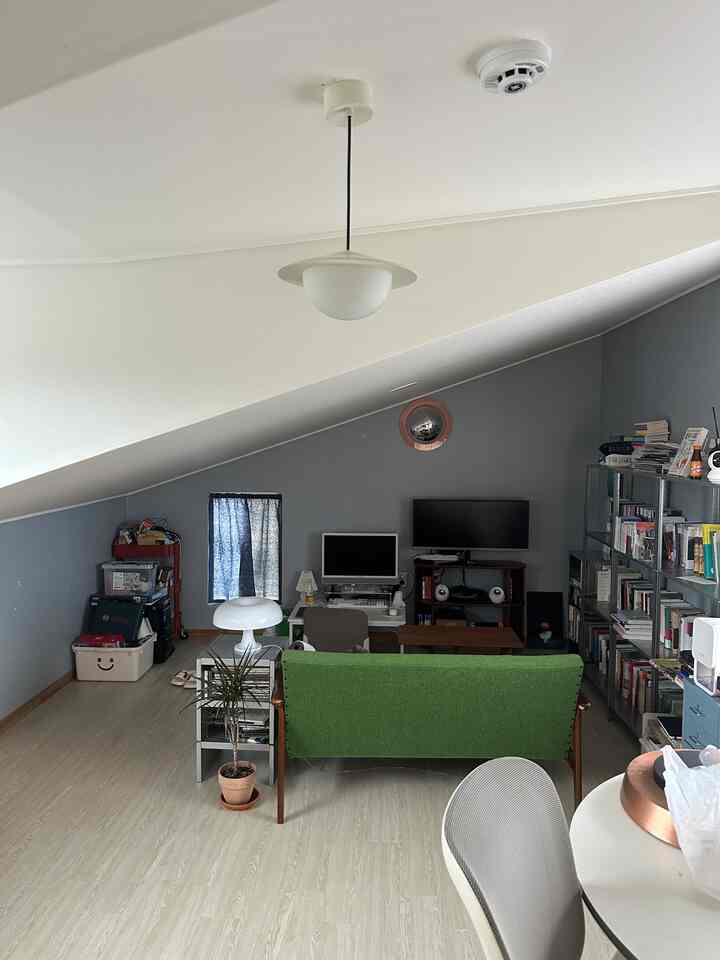 Natural color-toned study with slanted ceiling, featuring a green Garimoku sofa and pendant light in a cozy workspace