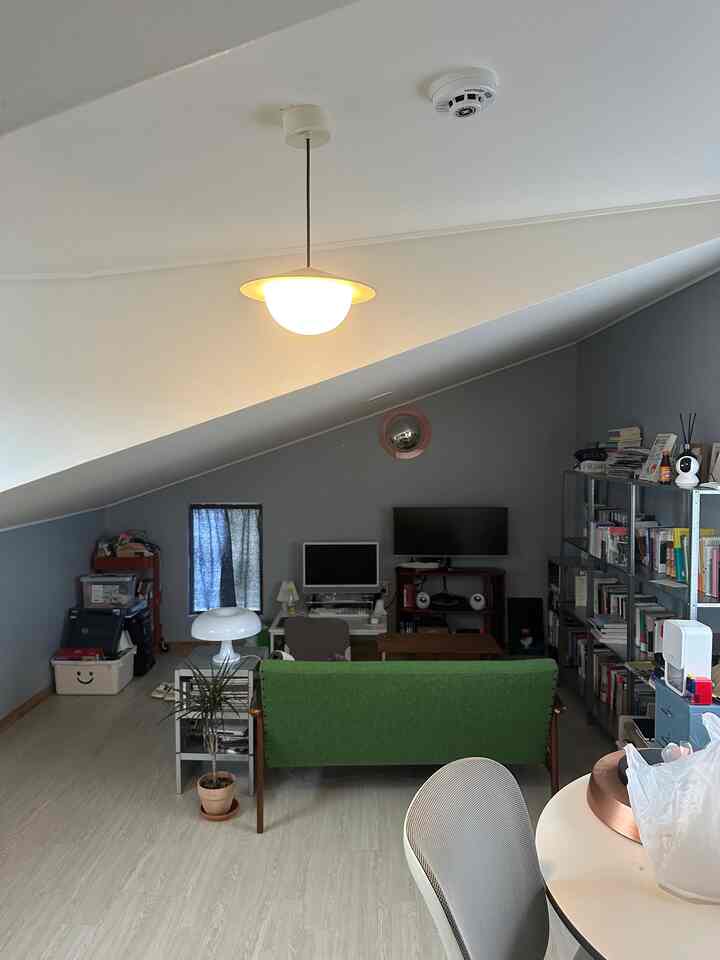 Gray and white toned small room with low slanted ceiling, featuring green sofa, desk, and bookshelf in a Nordic style home office
