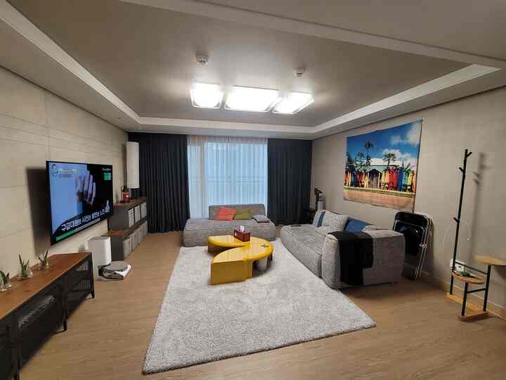 ネイビーのカーテンと黄色のコーヒーテーブルがあるモダンなリビング、グレーのソファと壁掛けテレビが配置された落ち着いた空間