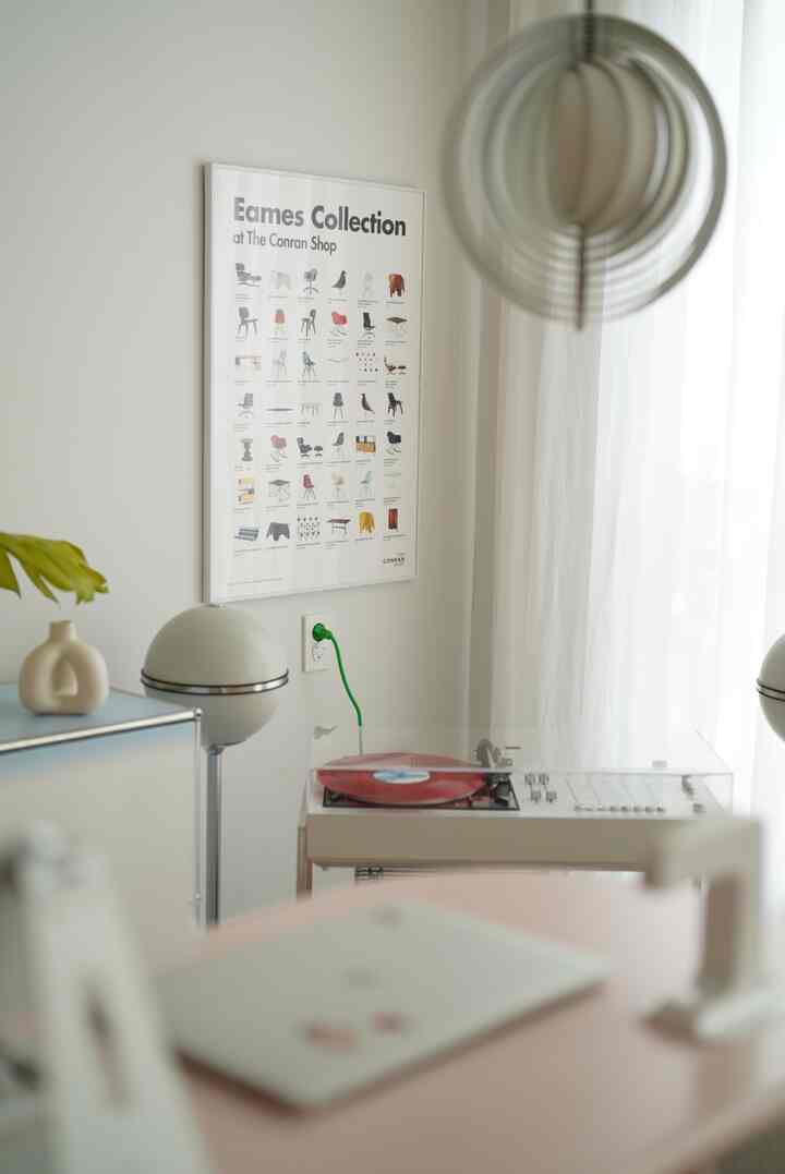 白色のリビング、白いカーテンとポスター、ミニマルな家具と照明が配置された空間